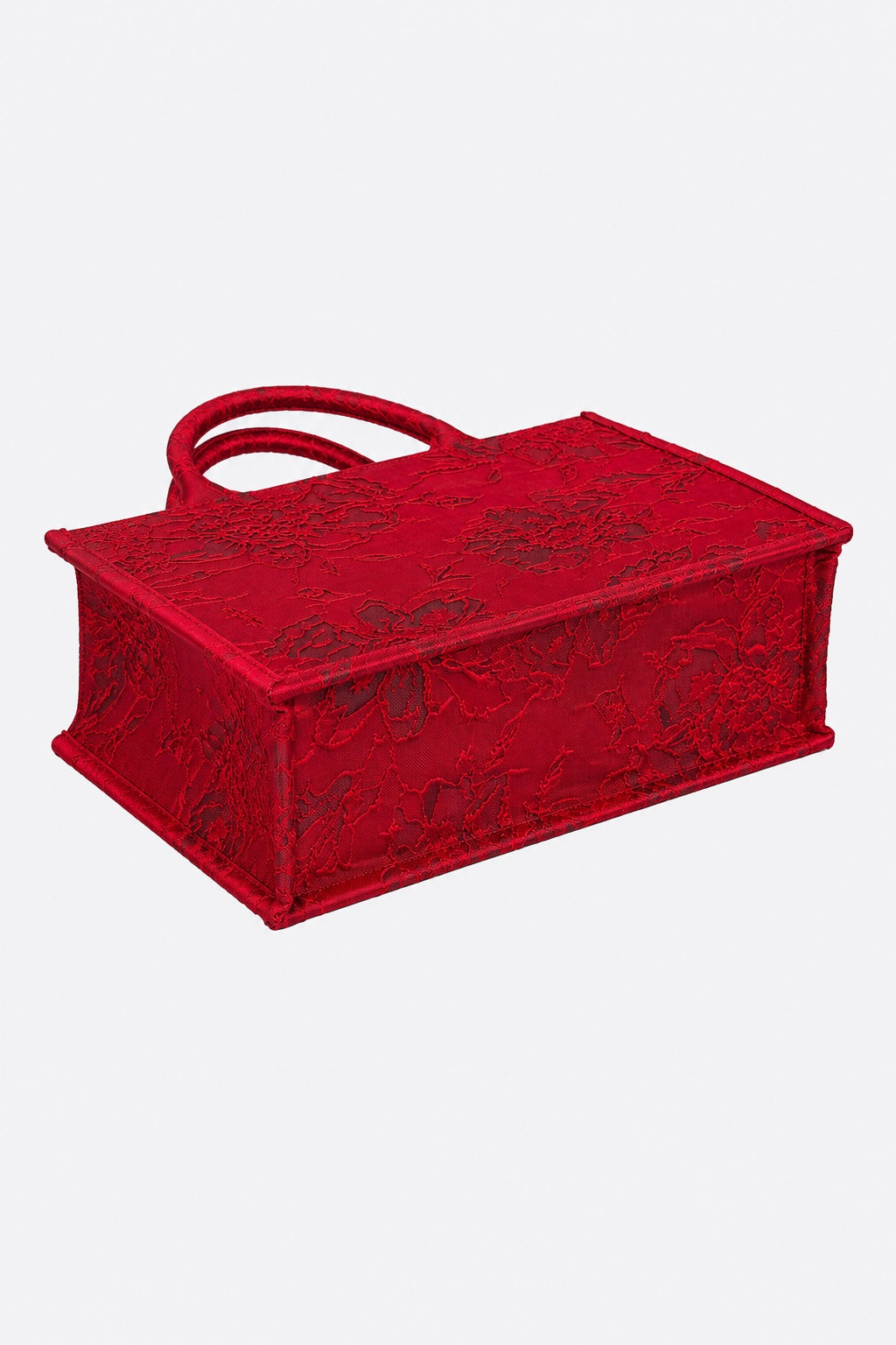 A red rectangular handbag with a matching top handle, featuring an intricate tonal floral lace pattern on the front and sides, shown against a plain light gray background.