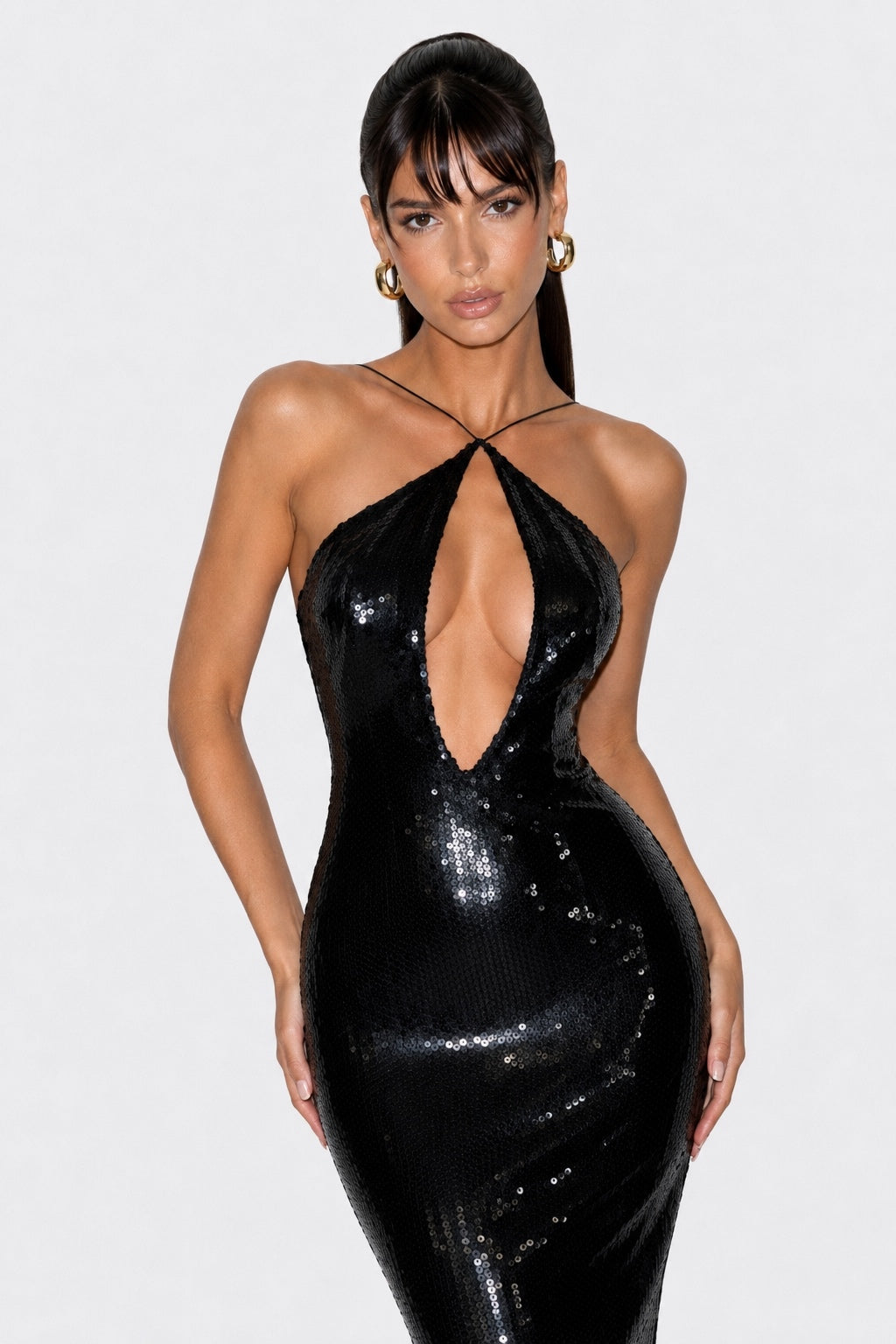 A woman shown from the back wearing a floor-length black sequined gown with a deep open back, photographed against a light gray studio background.