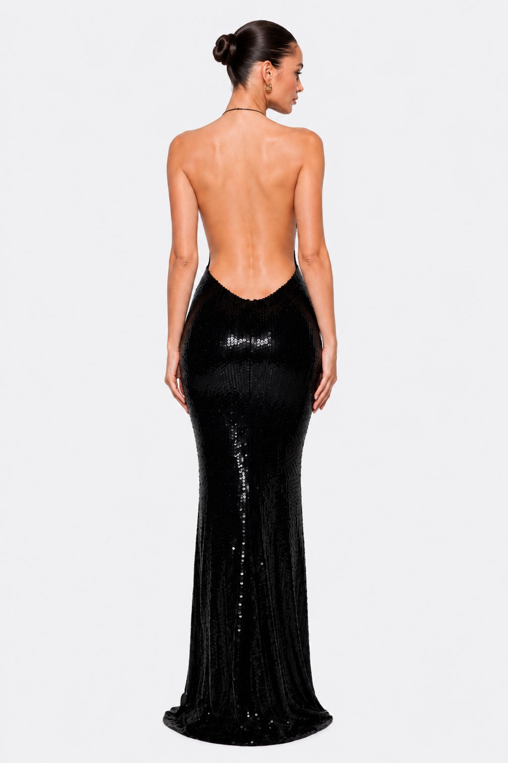 A woman shown from the back wearing a floor-length black sequined gown with a deep open back, photographed against a light gray studio background.