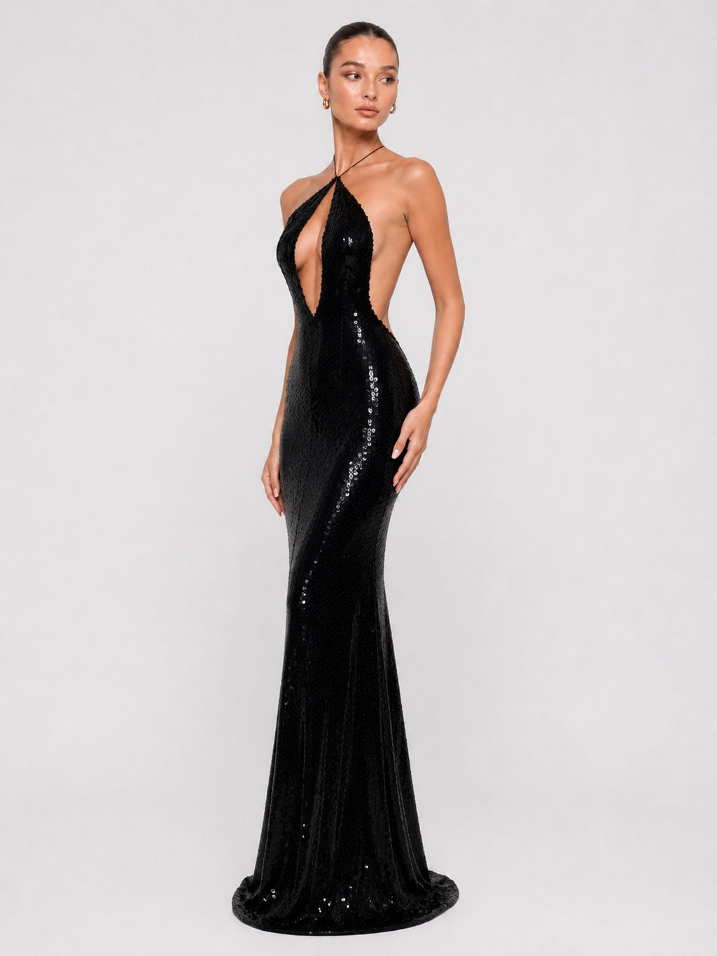 A model wearing a floor-length black sequined halter gown with a plunging cutout front and side cutouts, photographed against a light gray studio background.