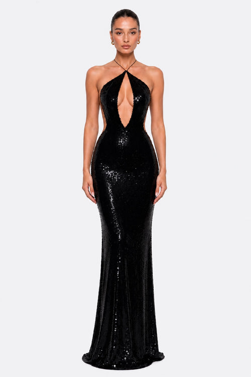 A model wearing a floor-length black sequined gown with a halter neckline, plunging cutout at the bust, and a fitted silhouette that flares slightly at the hem, photographed against a light gray studio background.