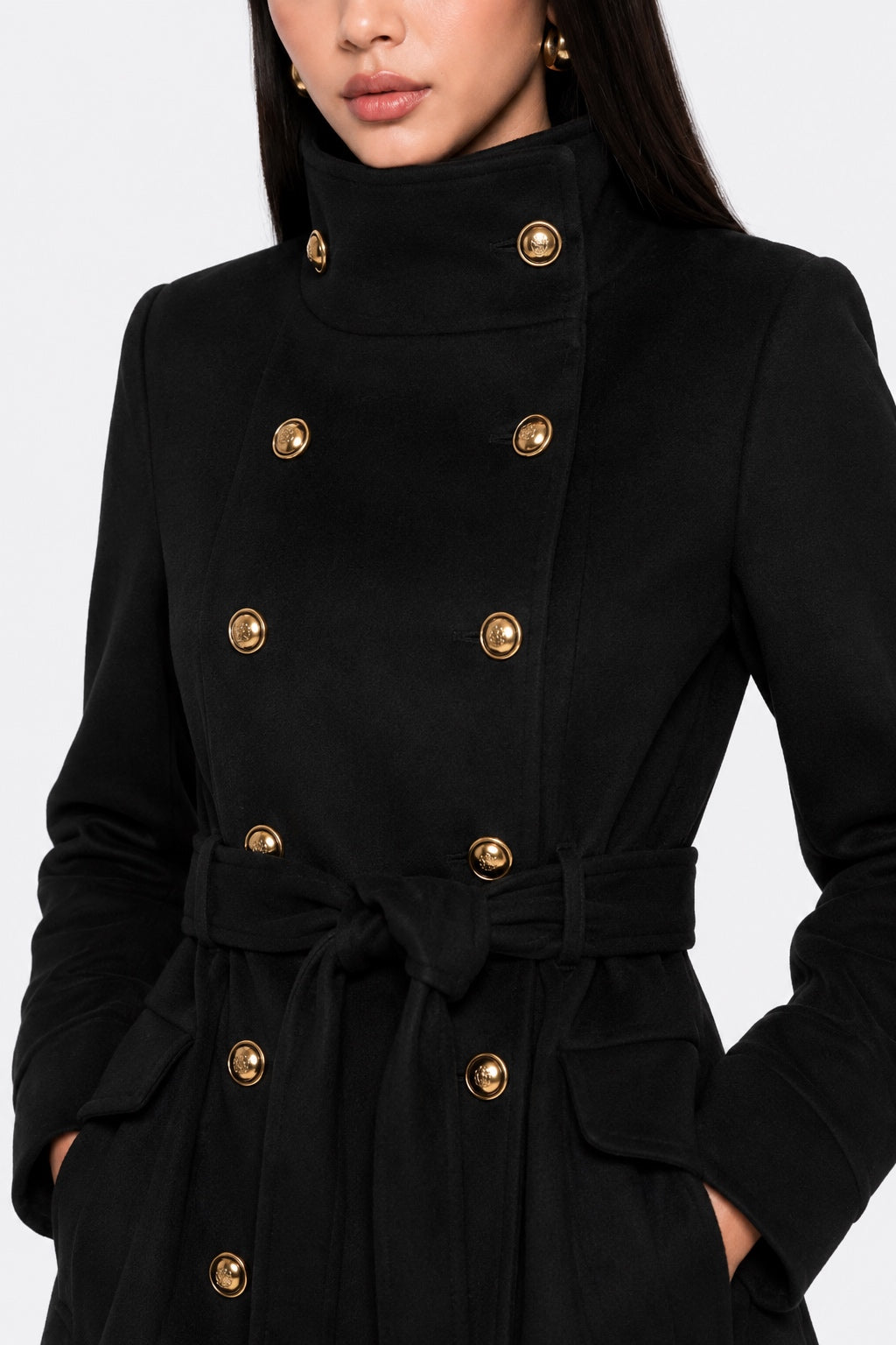 A close-up of a model wearing a black double-breasted belted coat with prominent gold-tone buttons.