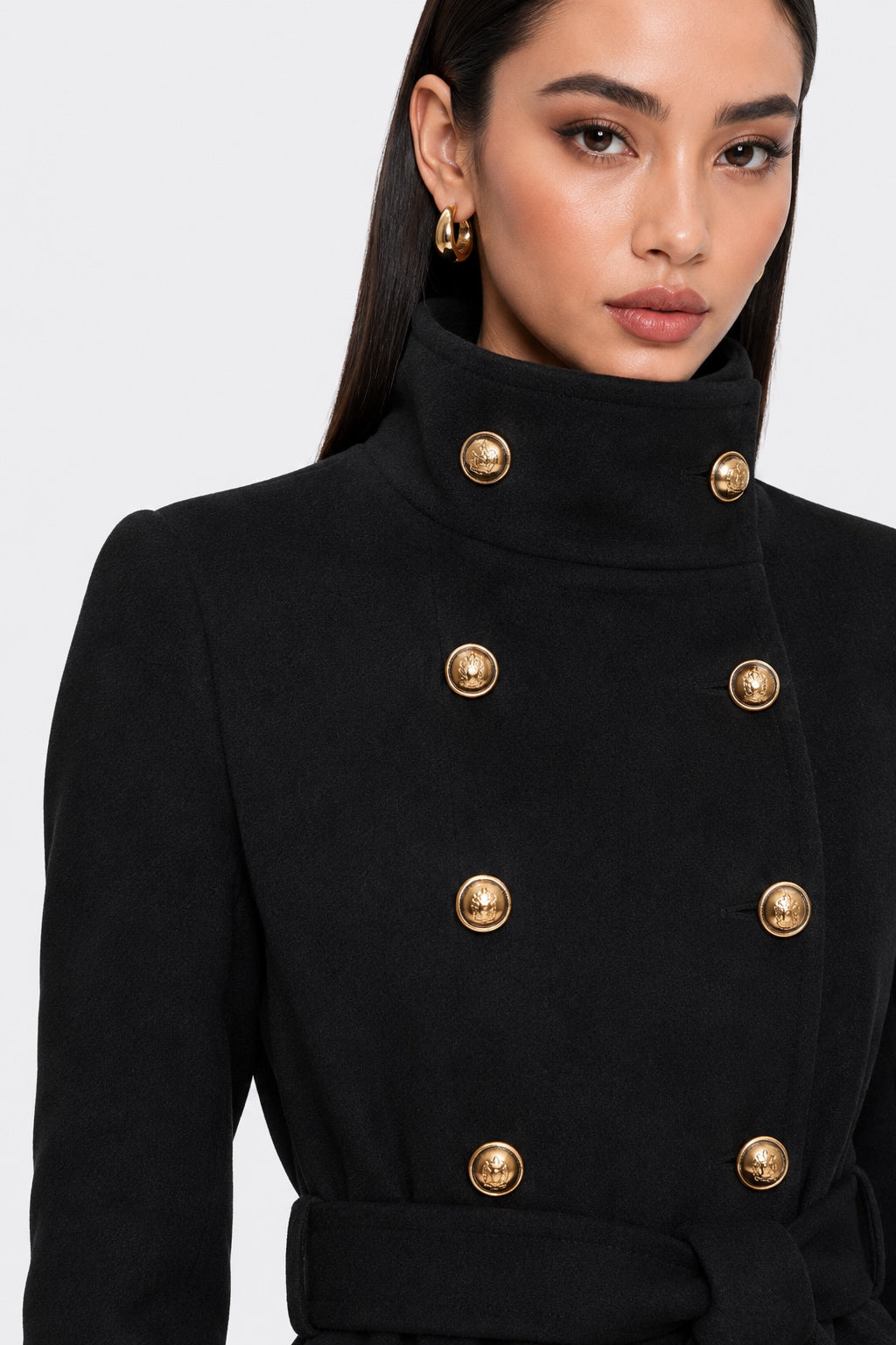 A close-up of a model wearing a black double-breasted coat with prominent gold buttons and a high mock neck collar.