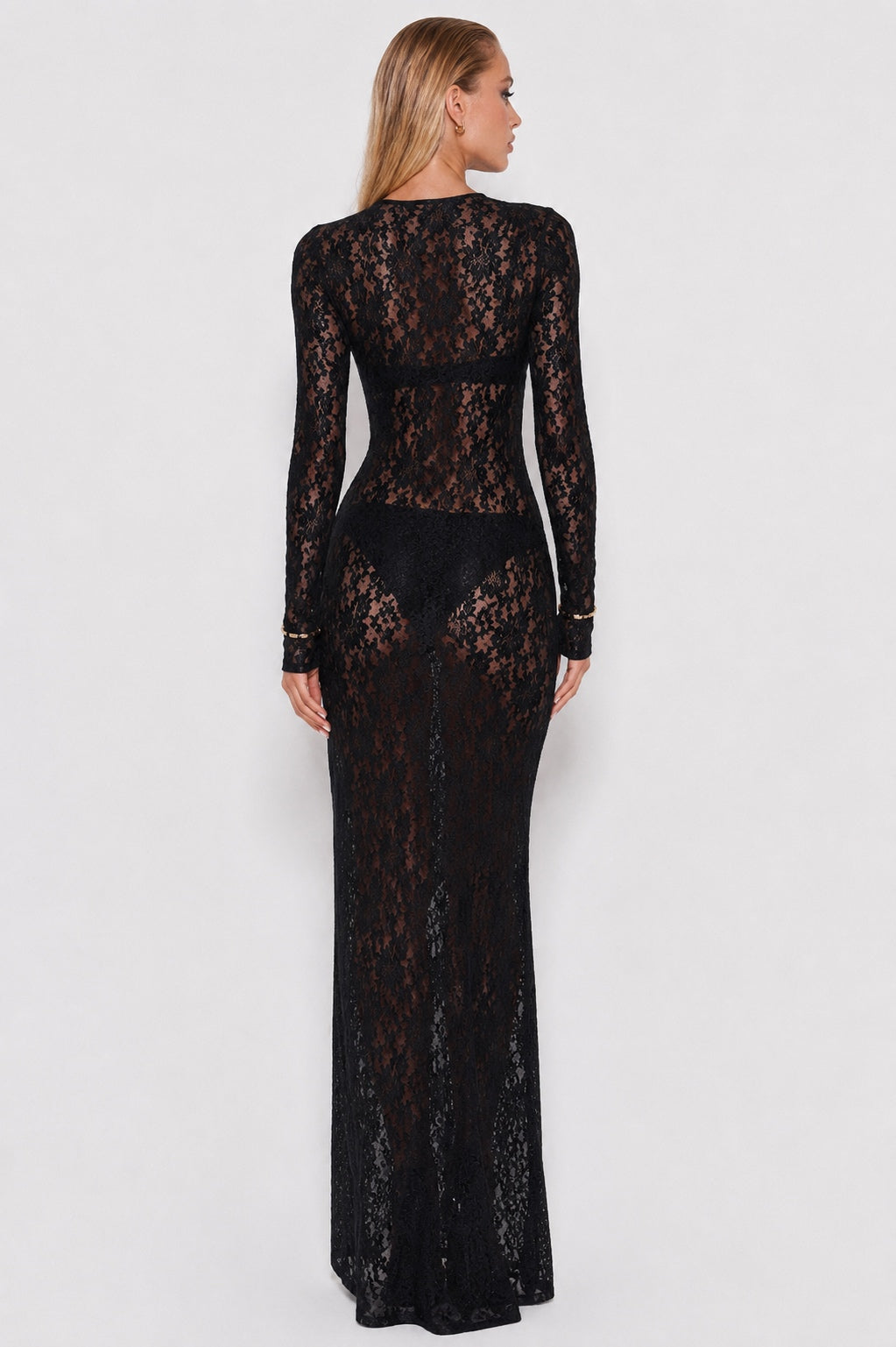 A woman modeling a long-sleeve black lace maxi dress from the back, shown against a plain light gray studio background.