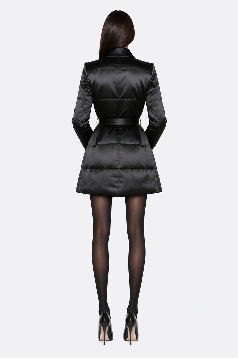 A model shown from the back wearing a black satin-like puffer jacket with a matching belt, black tights, and black high heels against a light gray studio background.
