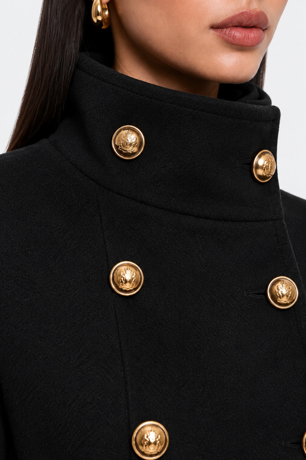 Close-up of a black double-breasted coat with ornate gold buttons and a high collar, worn by a model.