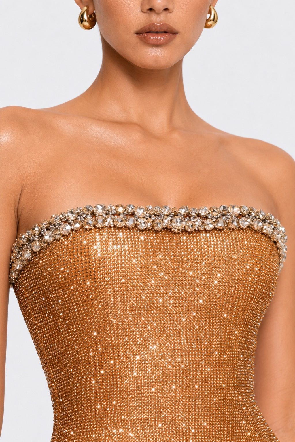 Close-up of a strapless gold sequined gown with a crystal-embellished sweetheart neckline, worn by a model against a light gray background.