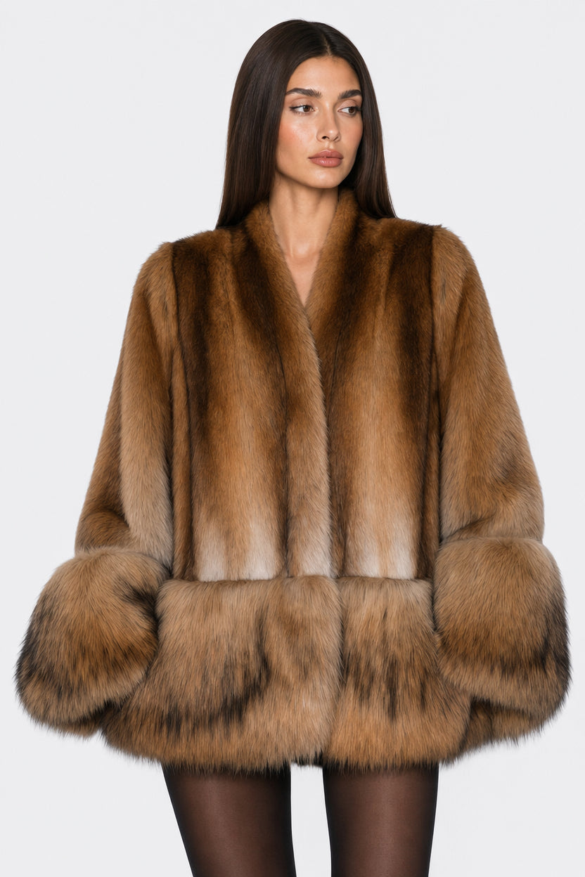 A woman modeling a luxurious brown fur coat with a shawl collar, voluminous sleeves, and a wide collar, set against a plain light gray background.