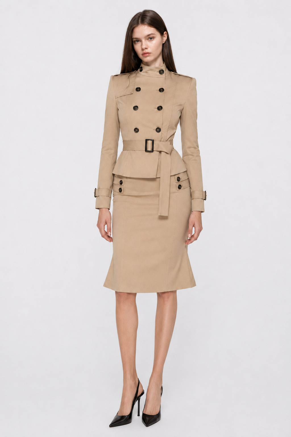 Female model standing front-facing in a full-length studio shot wearing a camel double-breasted trench jacket and matching midi skirt set with a defined belted waist.