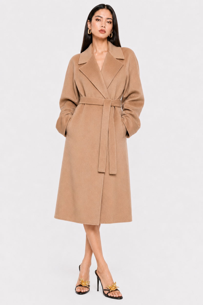 A woman modeling a camel-colored wool coat with a matching waist tie belt, styled with black strappy heels against a light gray studio background.