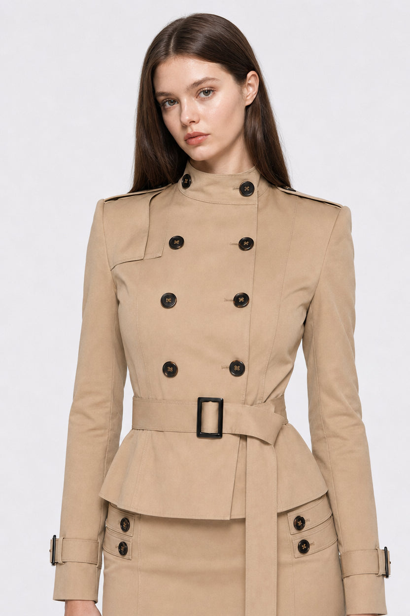 Female model in a front-facing portrait wearing a camel double-breasted trench jacket, belted at the waist with high collar and black button details.