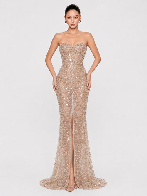 A woman modeling a strapless champagne sequined gown with a sweetheart neckline, fitted silhouette, thigh-high slit, and floor-length train against a light gray studio background.