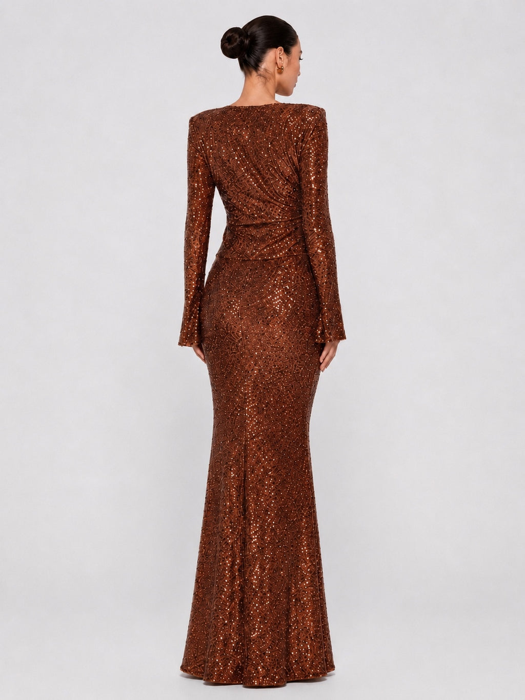 A woman modeling a floor-length copper-brown sequined gown from the back, shown against a plain light gray studio background.