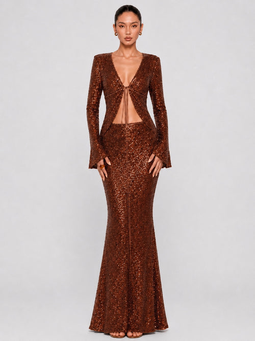 A model wearing a floor-length, sparkly bronze-brown sequined gown with long sleeves, a deep V-neckline, and a front cutout, photographed against a light gray studio background.