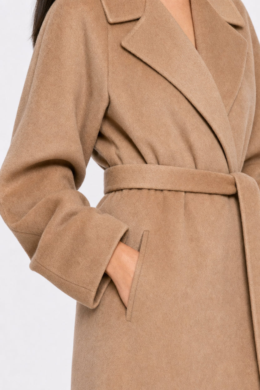 A close-up of a person wearing a camel-colored belted coat with a side pocket, shown against a plain light background.