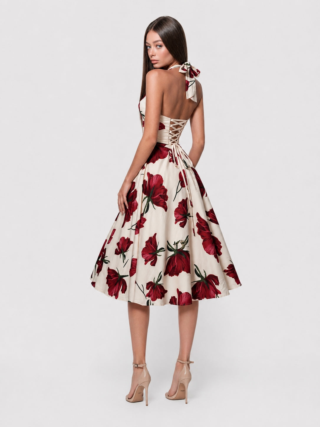 A woman modeling a sleeveless A-line midi dress with a cream base and a bold red floral print, shown from the back against a light gray studio background.