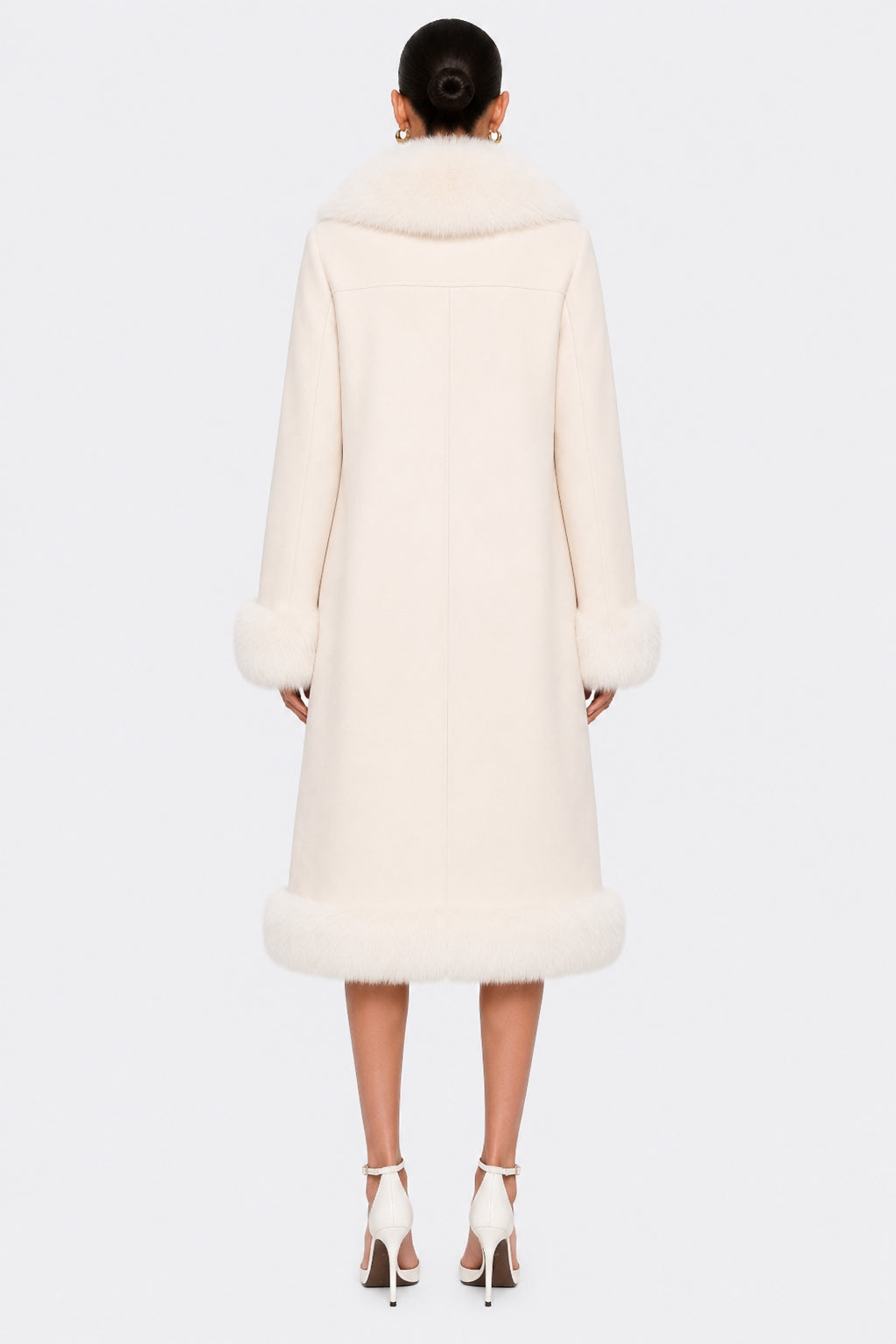 A model viewed from the back wearing a long cream-colored natural fur coat with a high collar, wide cuffs, and a fluffy trim at the hem, paired with white high-heeled sandals against a light gray background.