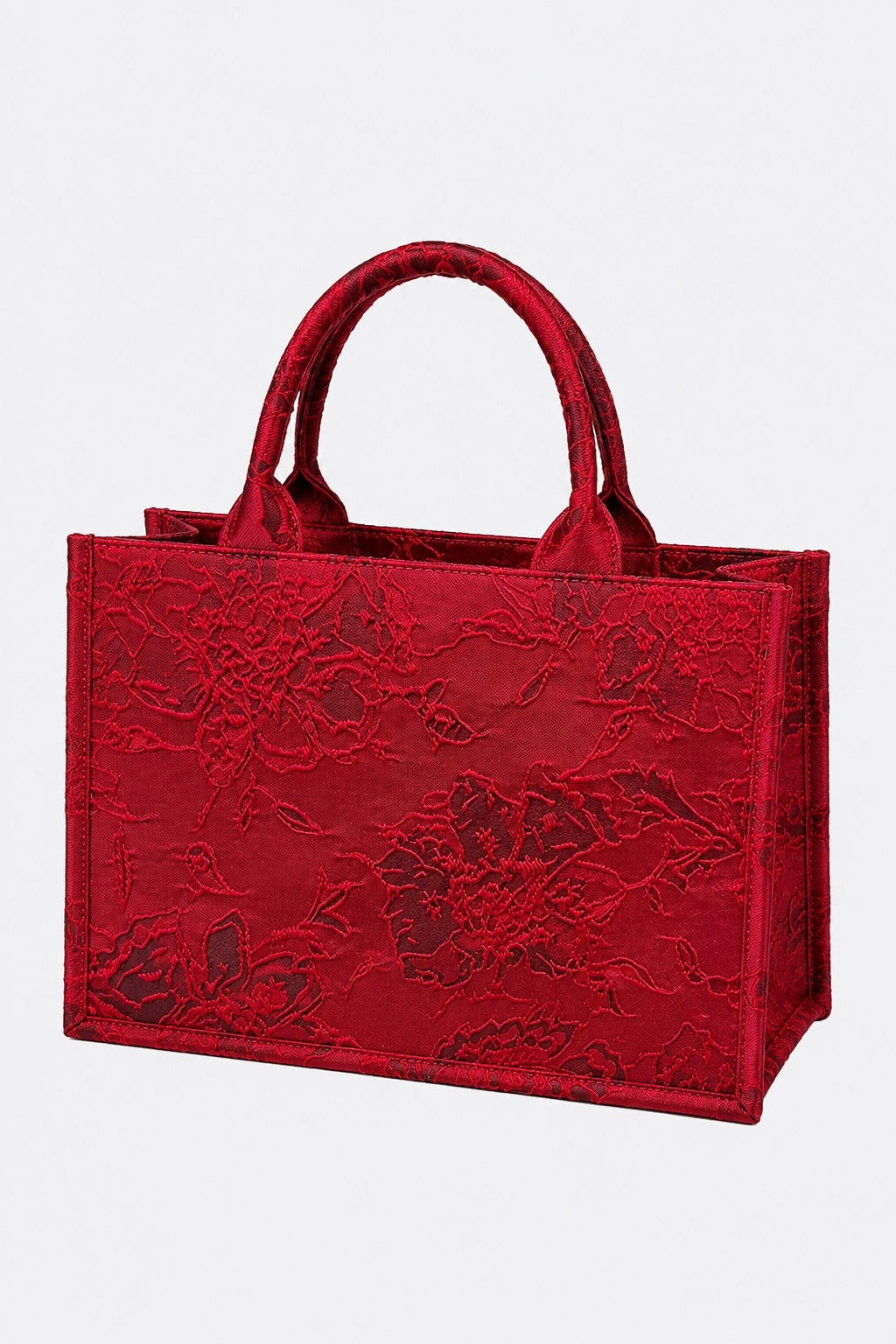 A red textured tote bag with floral jacquard detailing and double top handles, shown against a plain light gray background.