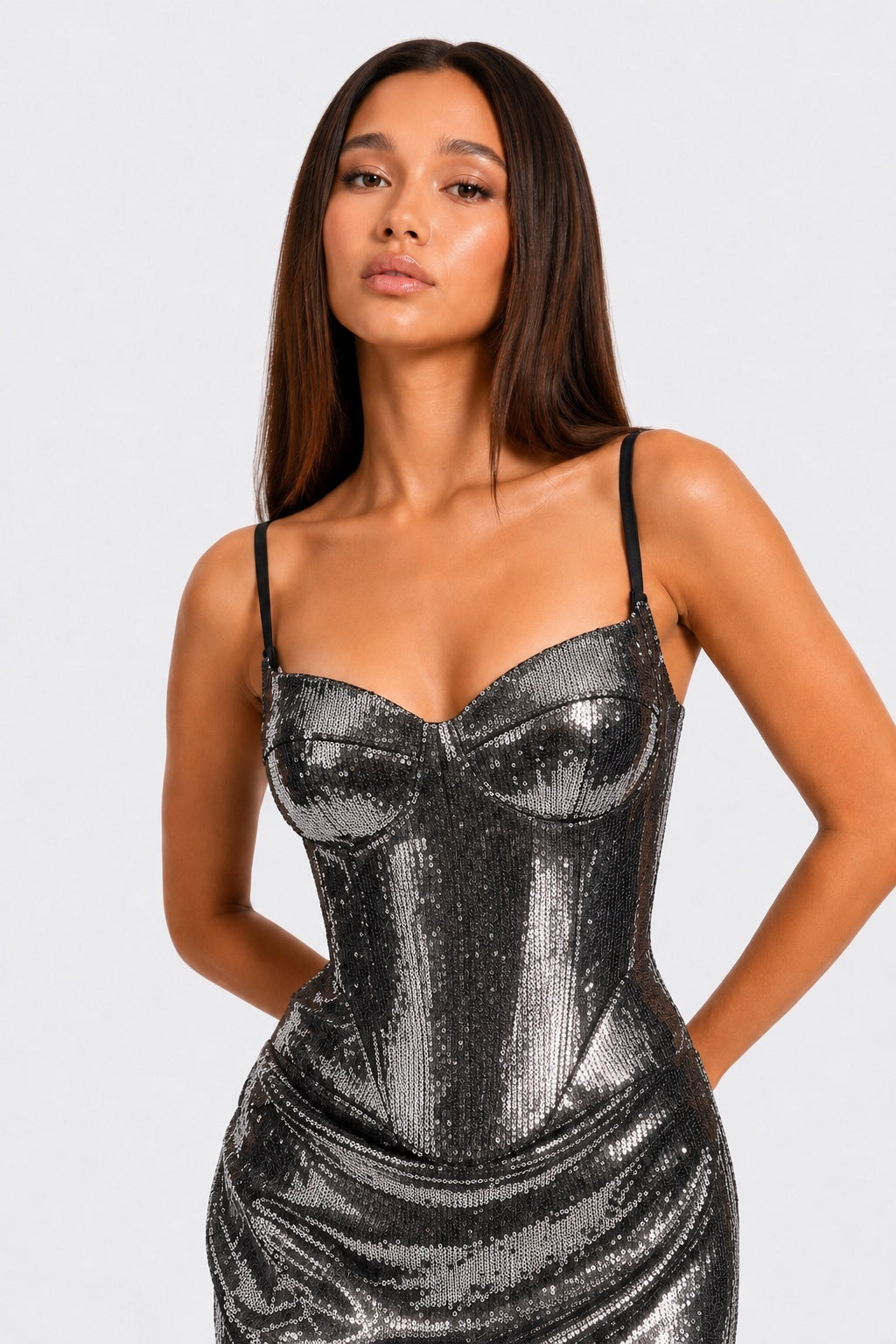 A woman modeling a shimmering silver sequin spaghetti-strap dress against a light gray studio background.