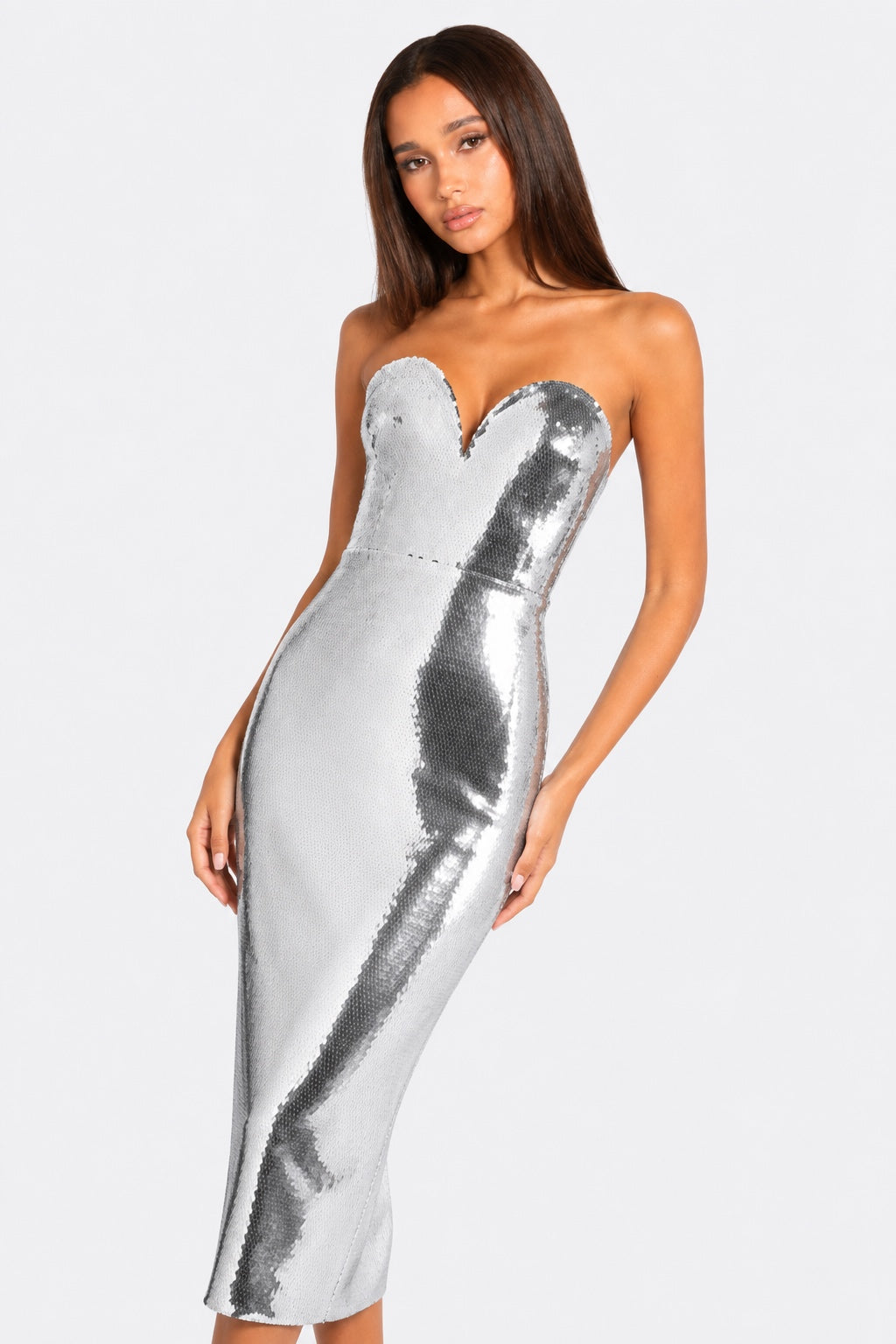 A woman modeling a strapless silver sequin midi dress with a sweetheart neckline against a light gray studio background.