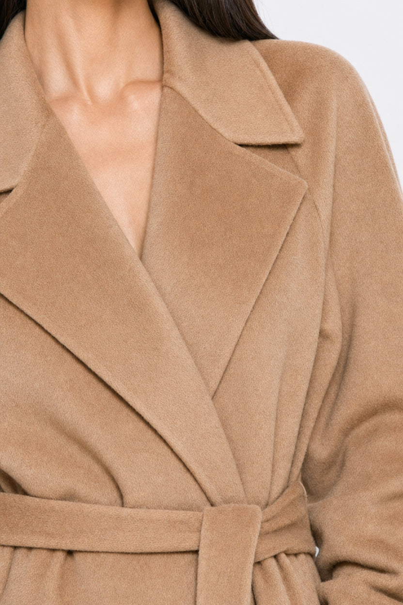 Close-up of a model wearing a camel-colored belted coat with wide lapels and a soft, matte texture.