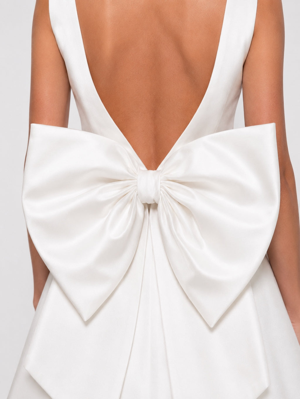 Close-up back view of a white satin dress with a large bow at the back, worn by a model.