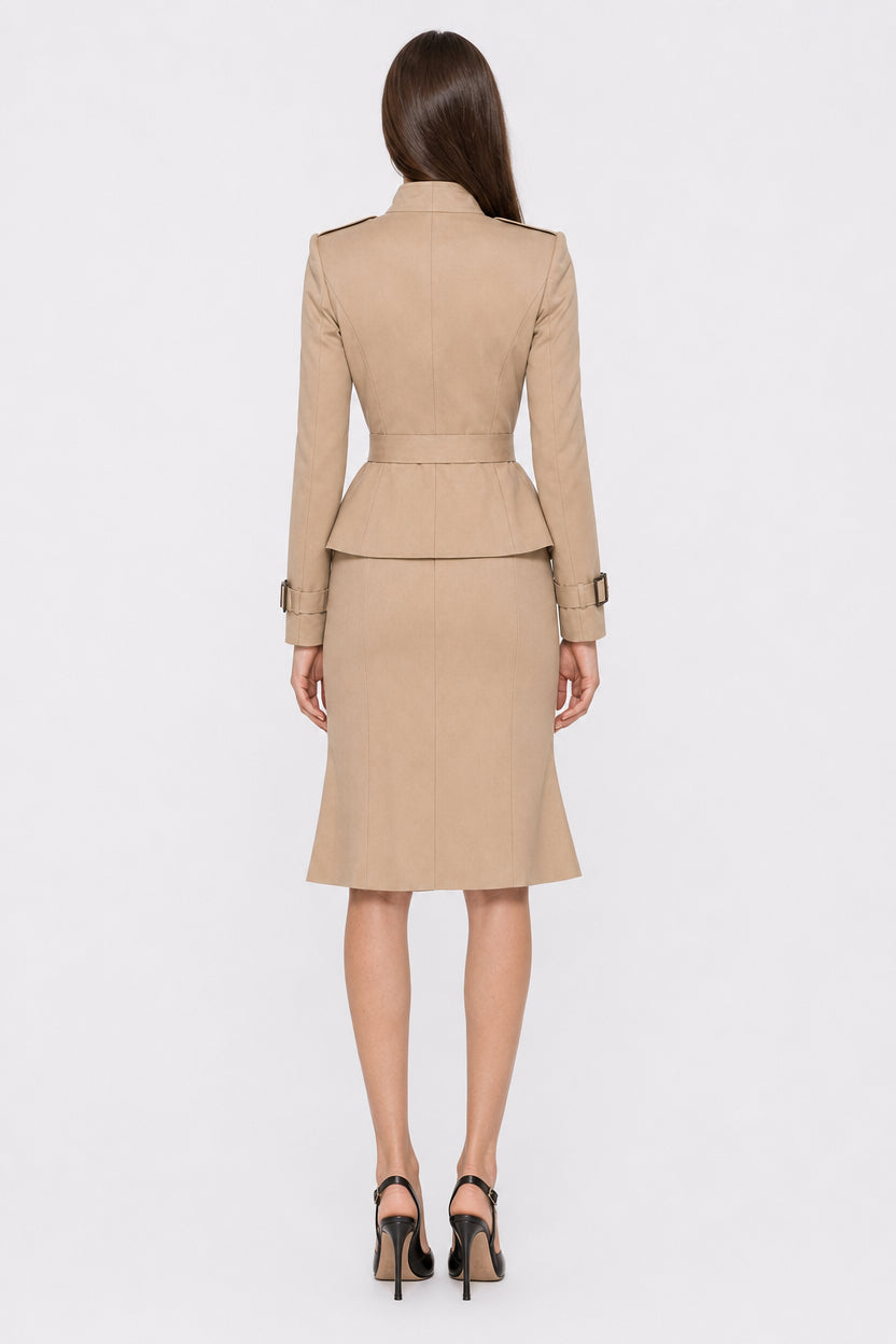 A woman viewed from the back wearing a beige tailored suit set consisting of a long-sleeve blazer with a peplum waist and matching knee-length skirt, paired with black high heels against a light gray studio background.